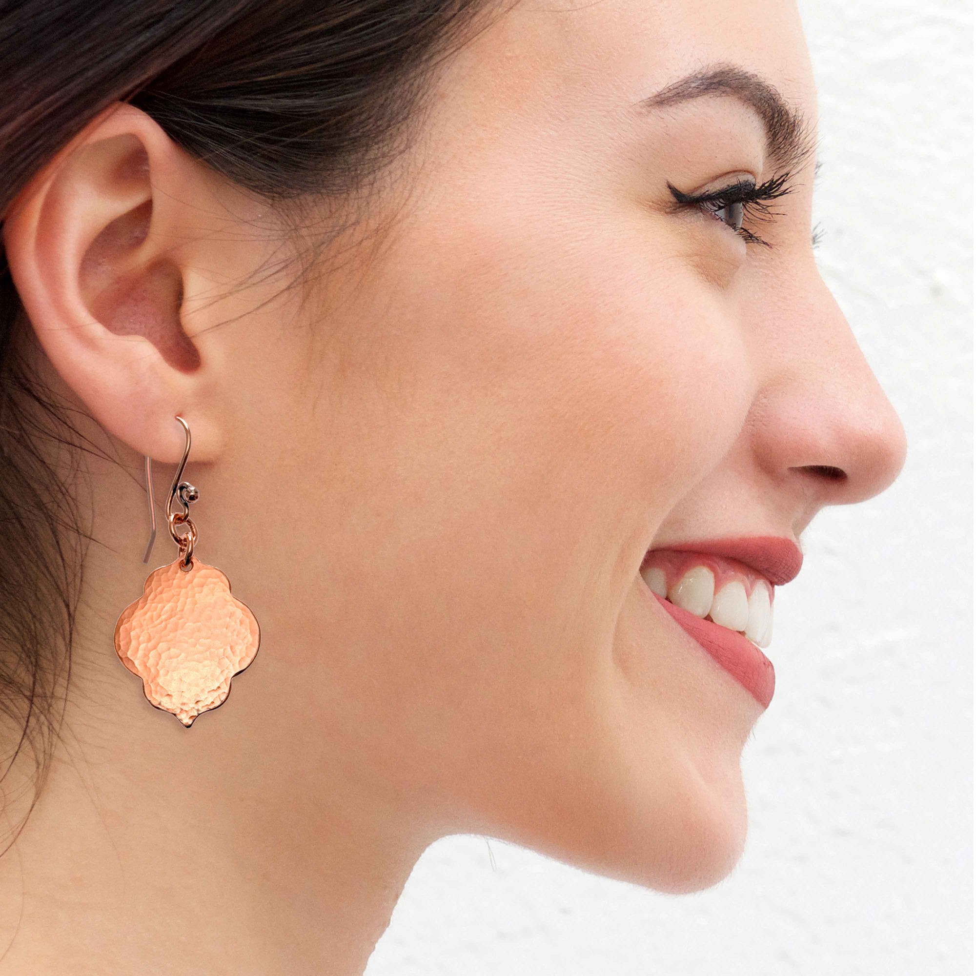 A Smiling Woman Wearing Small Hammered Copper Quatrefoil Dangle Earrings