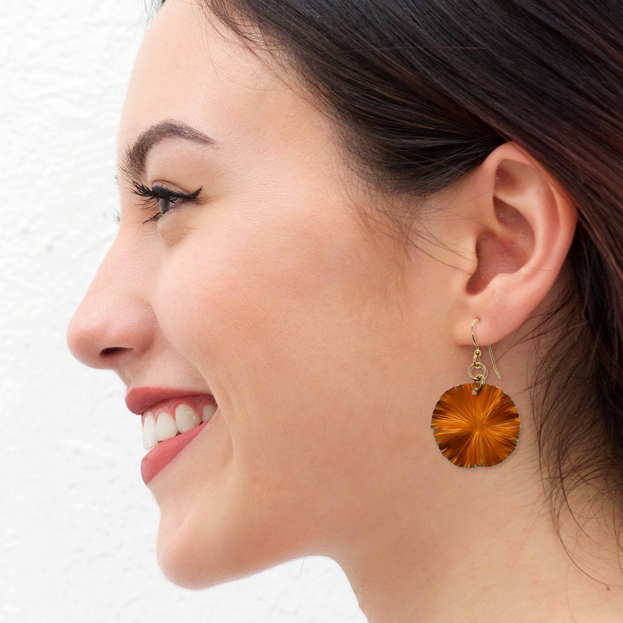 Woman wearing orange lily pad earrings with gold hooks.